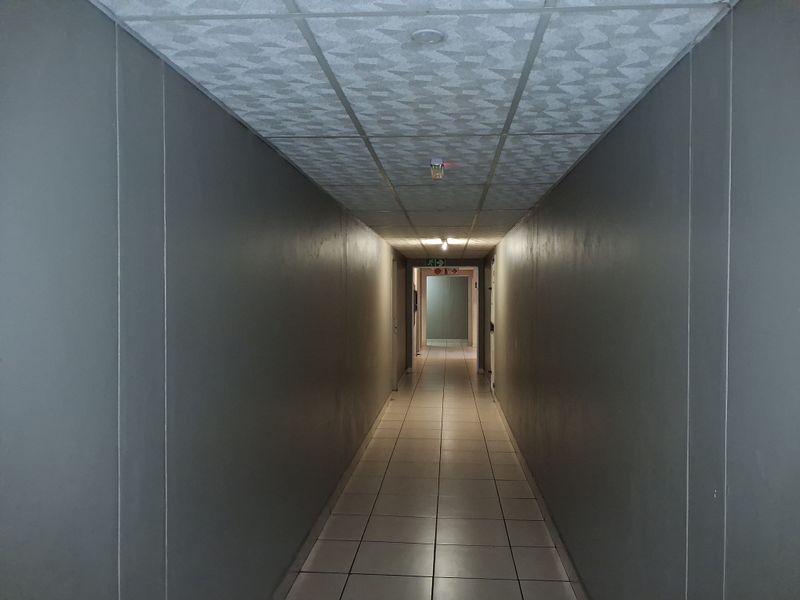 A long, empty apartment building hallway featuring tiled flooring and a drop ceiling with integrated lighting.
