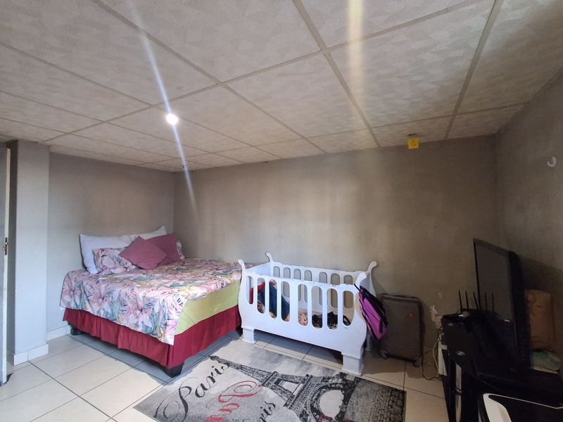 A bedroom featuring tiled flooring and a drop ceiling, currently requiring cosmetic updates to the wall finishes and ceiling structure.