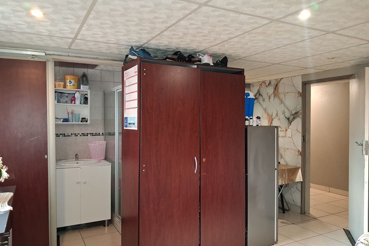 An interior space featuring tiled flooring, a drop ceiling with recessed lighting, a small vanity basin, and a shower enclosure.