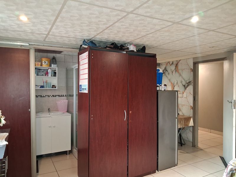 An interior space featuring tiled flooring, a drop ceiling with recessed lighting, a small vanity basin, and a shower enclosure.