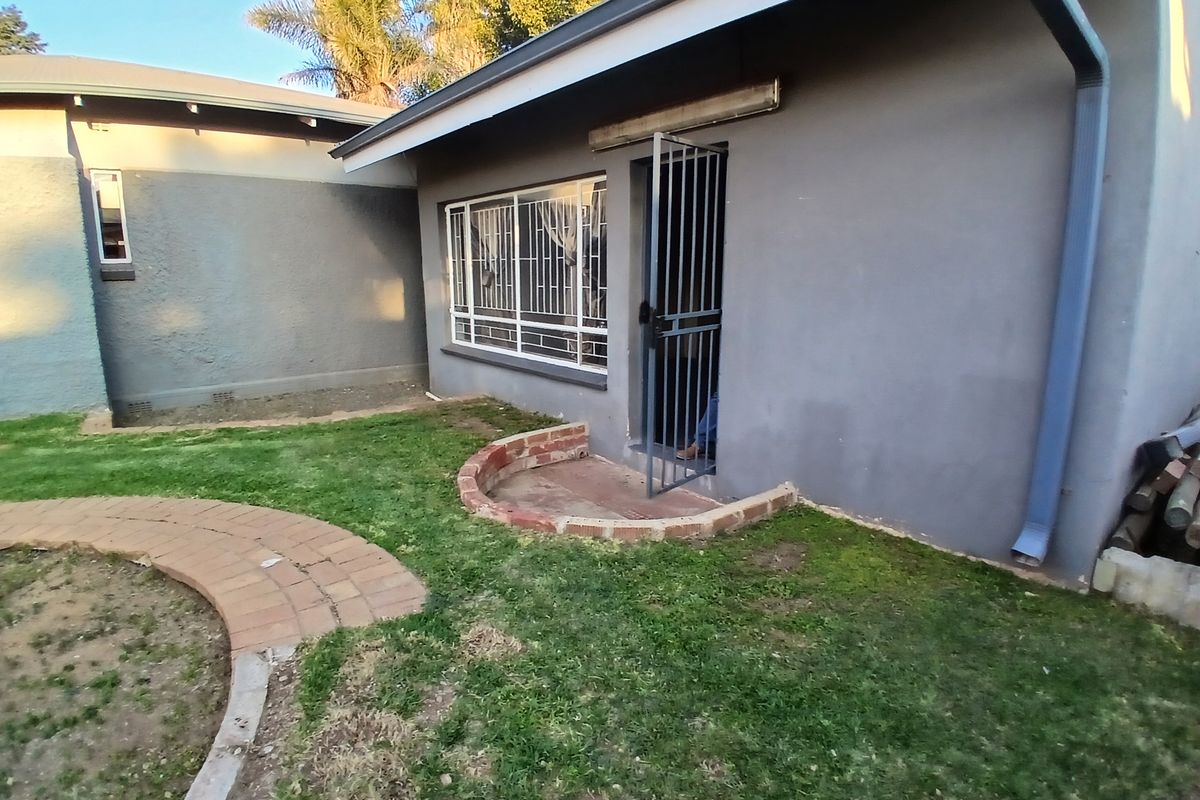 Rear exterior view of the property featuring a paved garden path, security gate, and security bars on the windows.