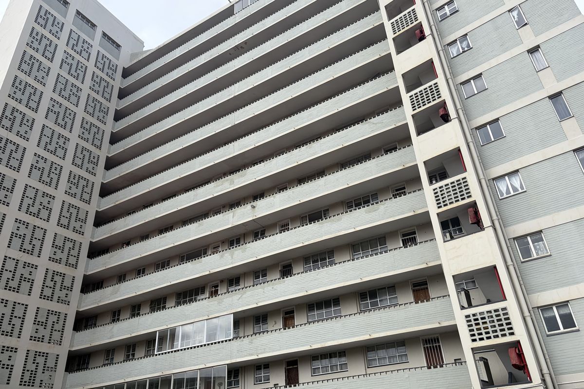 A low-angle view of a multi-story apartment building featuring a series of balconies, concrete facade, and decorative breeze block architectural detailing.
