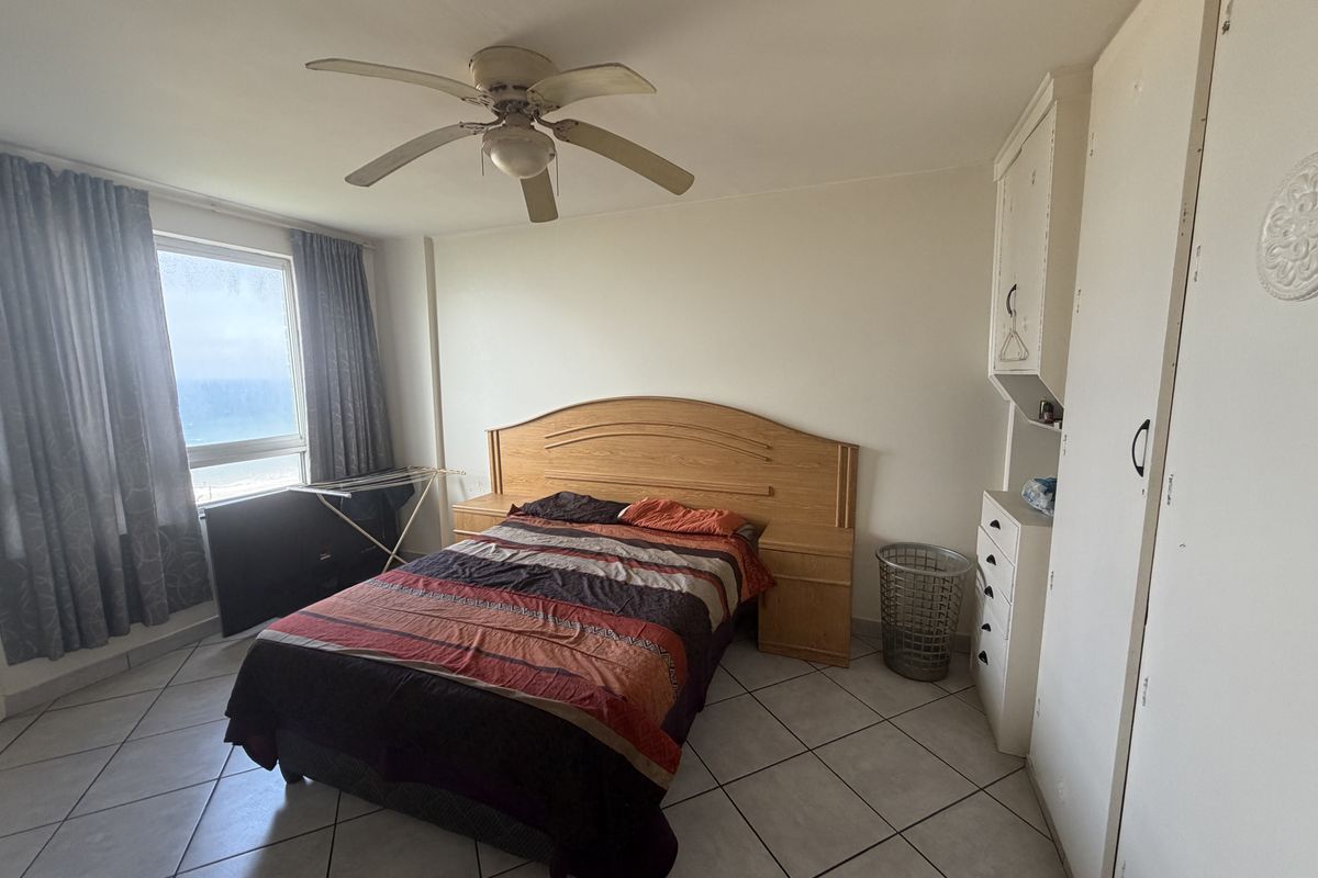 A bedroom featuring tiled flooring, a ceiling fan, and built-in cupboards with views of the ocean.