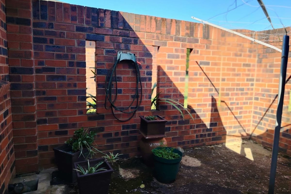 A private rear courtyard area featuring a brick boundary wall, concrete paving, and a rotary clothesline, offering potential for outdoor improvement.