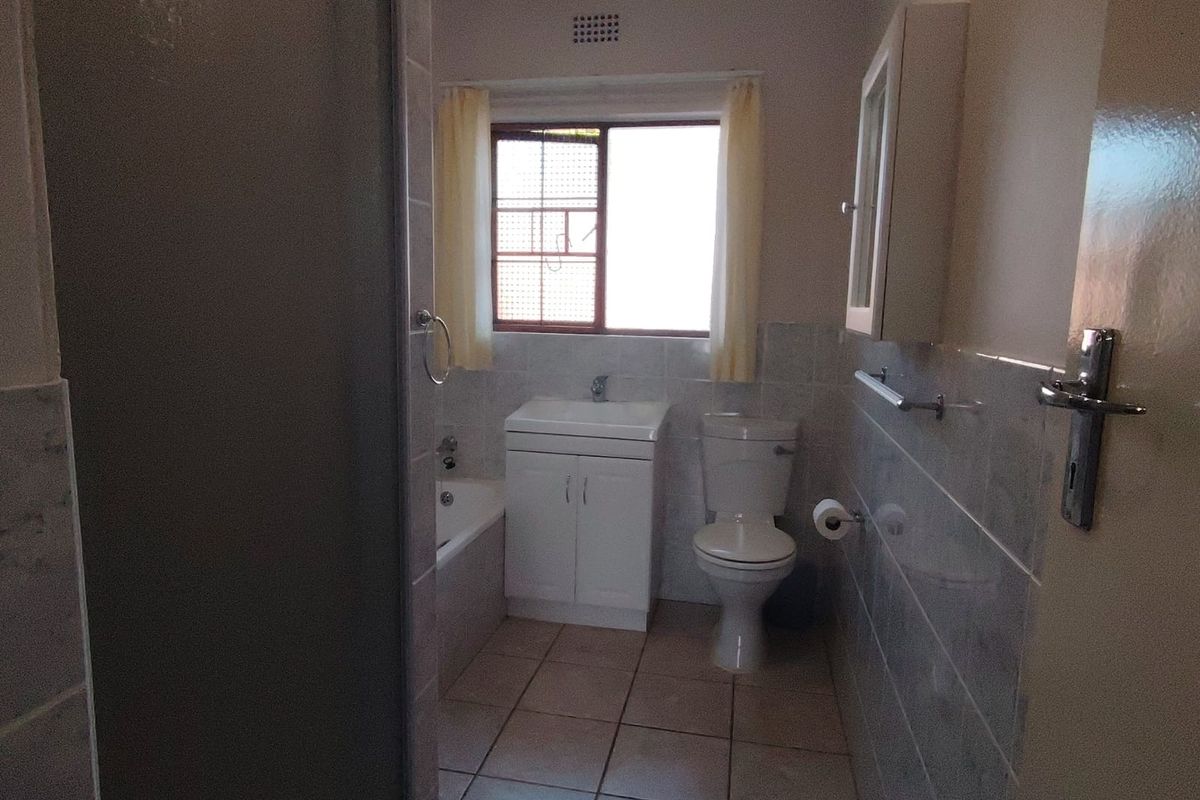 A functional bathroom featuring a shower enclosure, bathtub, vanity basin, and toilet with neutral wall and floor tiling.