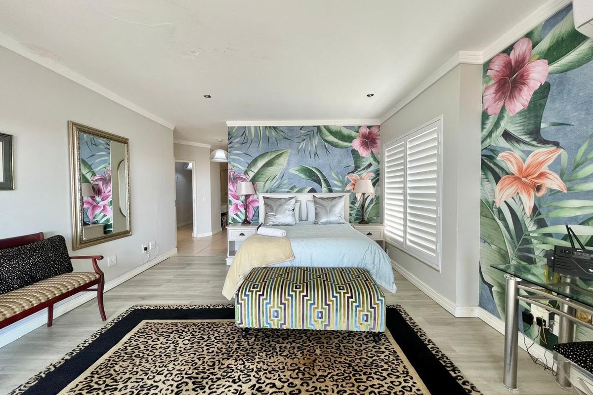 Spacious bedroom featuring laminate flooring, plantation shutters, and a decorative floral feature wall, providing a bright and well-maintained living space.
