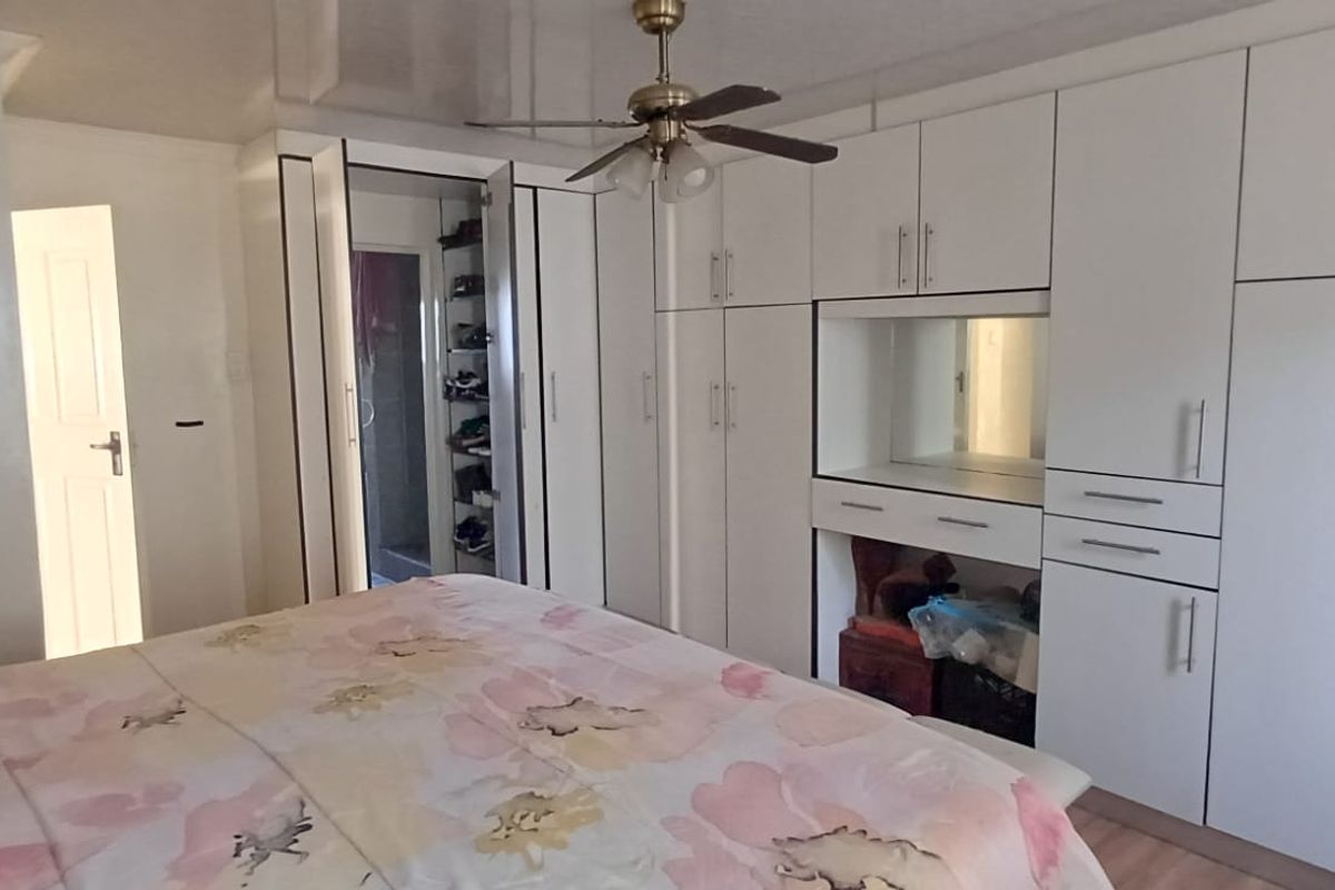 Spacious bedroom featuring extensive white built-in cabinetry, a central ceiling fan, and integrated vanity mirror with laminate flooring.