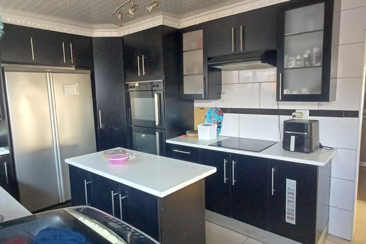 A functional kitchen featuring dark cabinetry, a central island, integrated oven, and tiled splashback, offering a practical layout for cooking and food preparation.