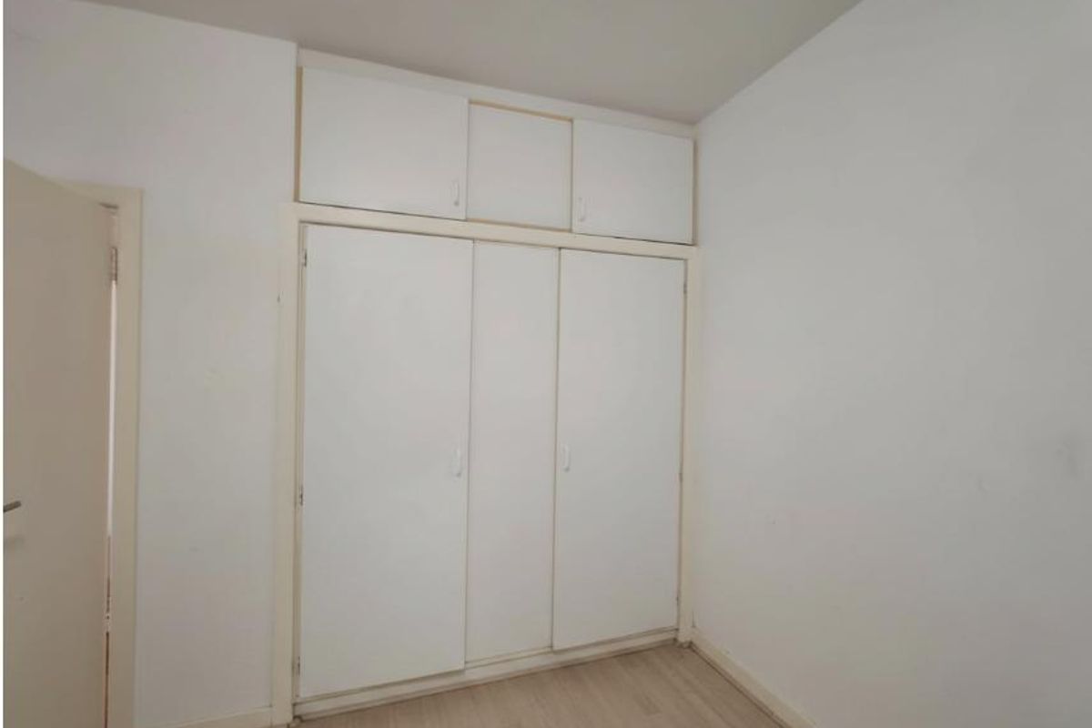 A vacant bedroom featuring white built-in wardrobes with overhead storage and light-toned laminate flooring.