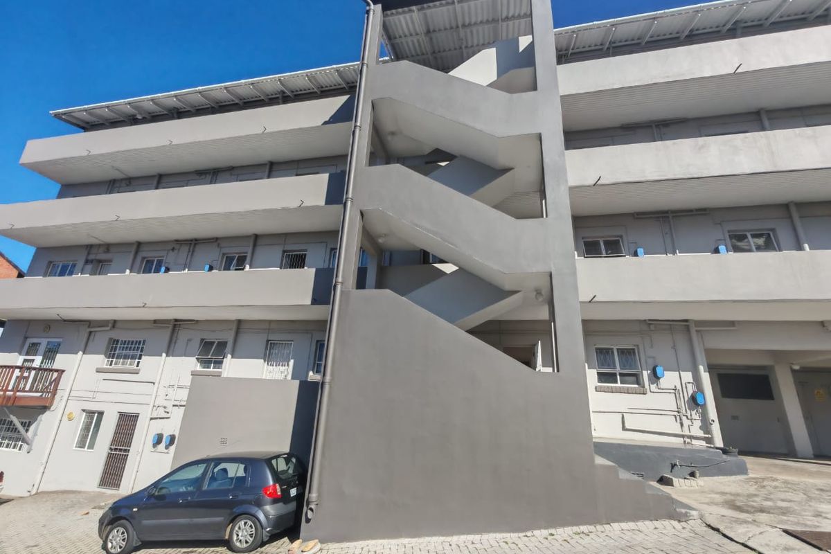 Exterior view of an apartment building featuring a prominent external staircase, paved driveway, and security-fitted windows and doors.