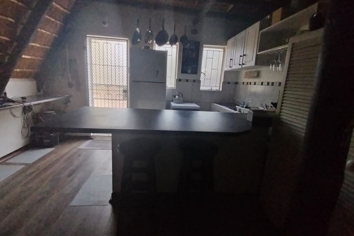 A rustic kitchen featuring an island, cabinetry, and exposed timber roof beams, with direct access to an exterior security door.