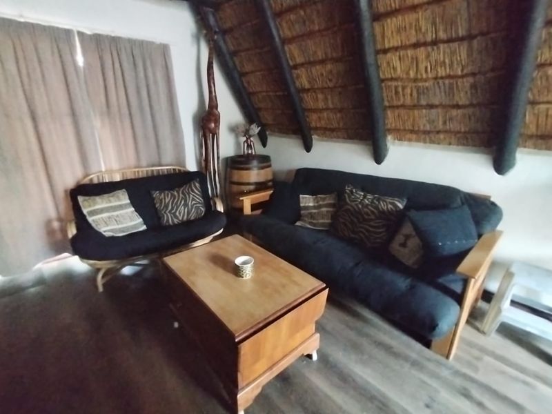 A cozy living room featuring a traditional thatched roof with exposed timber rafters and modern laminate flooring.
