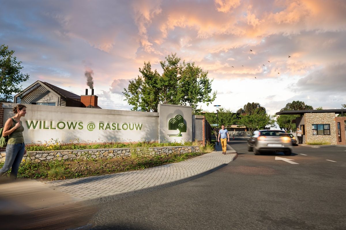 Entrance view of Willows @ Raslouw residential estate featuring a stone masonry wall, security booth, and paved access road.