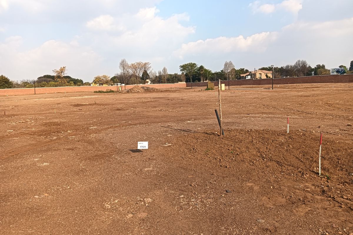 A vacant residential plot of land featuring level ground, boundary walling, and survey markers, ready for development.