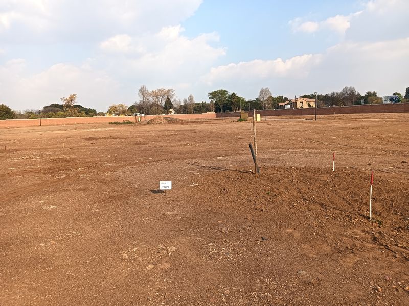 A vacant residential plot of land featuring level ground, boundary walling, and survey markers, ready for development.