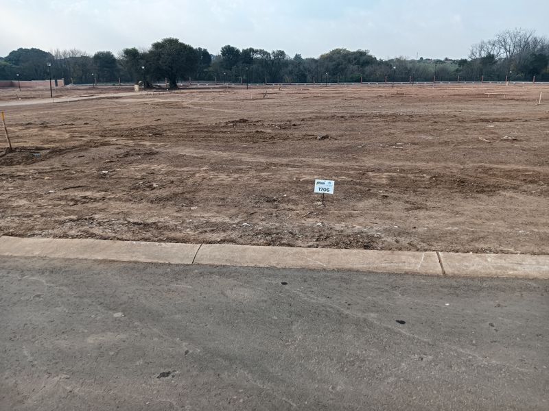 A vacant residential plot featuring a level surface, concrete curbing, and asphalt road access, ready for development.