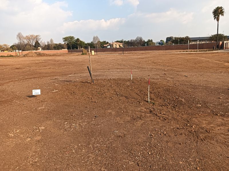 A vacant residential plot featuring clear survey markers and boundary pegs, ready for development in a residential estate.