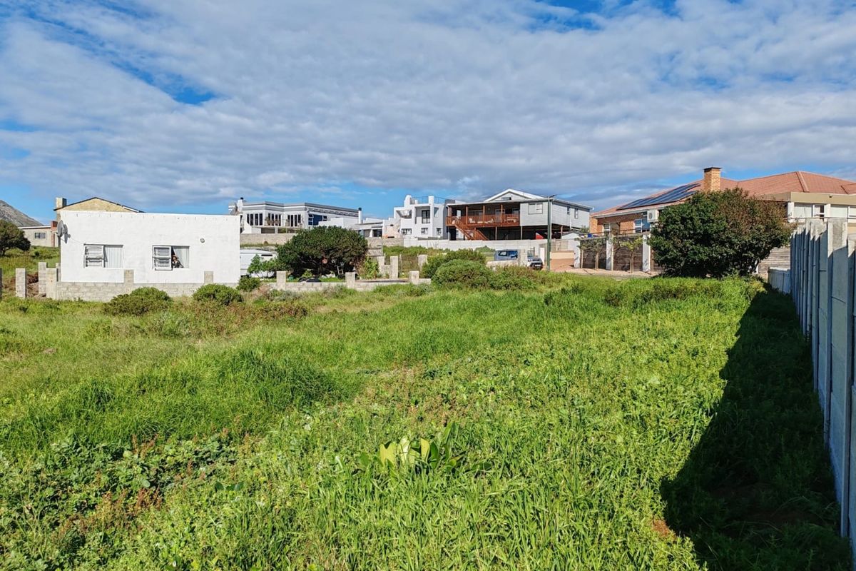 A vacant residential plot featuring overgrown grass and boundary walling, situated in a developed neighbourhood.