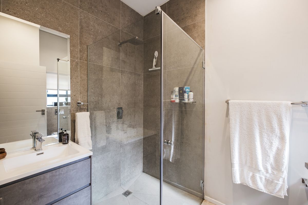 Modern bathroom featuring a sleek vanity, large wall mirror, and a spacious walk-in shower with a rainfall shower head and contemporary tiling.