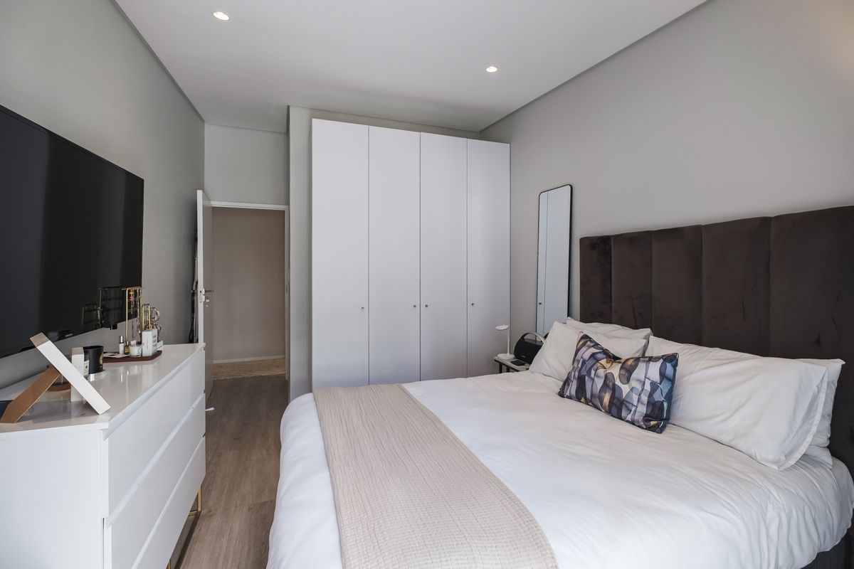 A well-maintained bedroom featuring built-in cupboards, recessed downlighting, and modern laminate flooring, offering a clean and functional living space.