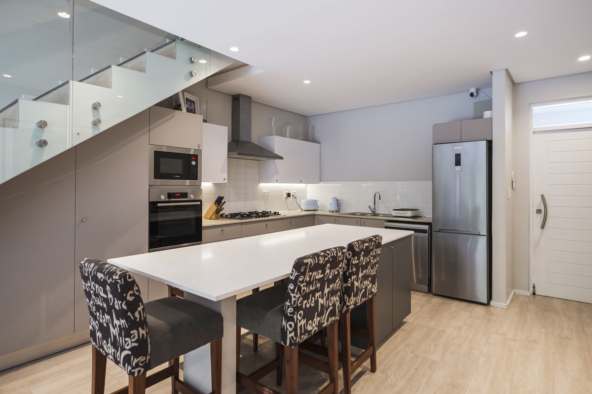 Modern kitchen featuring a central island, built-in appliances, sleek cabinetry, and a glass-railed staircase, creating a contemporary and functional open-plan living space.