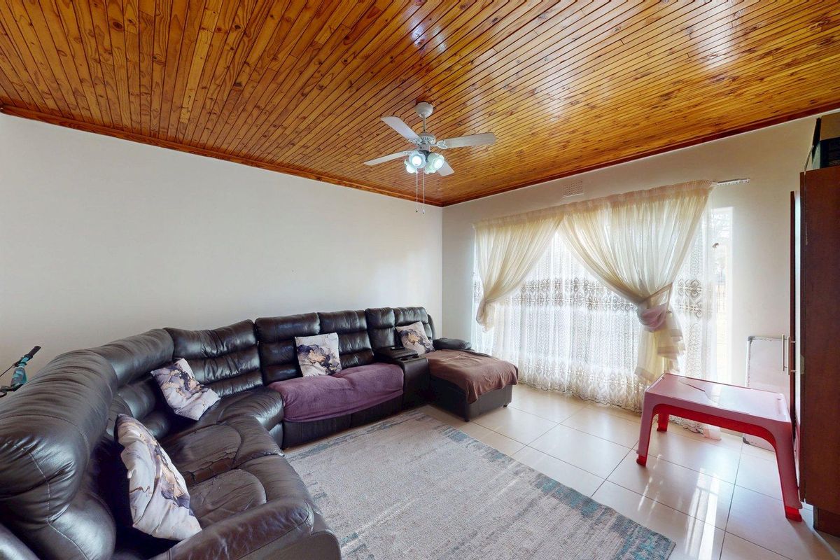 A living room featuring a warm timber tongue and groove ceiling, tiled flooring, and a large sliding glass door providing natural light.
