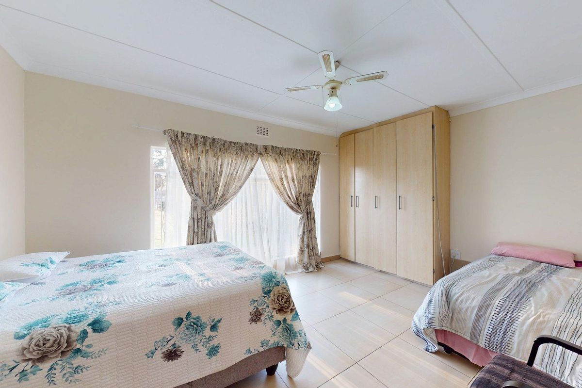 Spacious bedroom featuring neutral tiled flooring, built-in wooden cupboards, and a ceiling fan, offering a functional and well-lit living space.