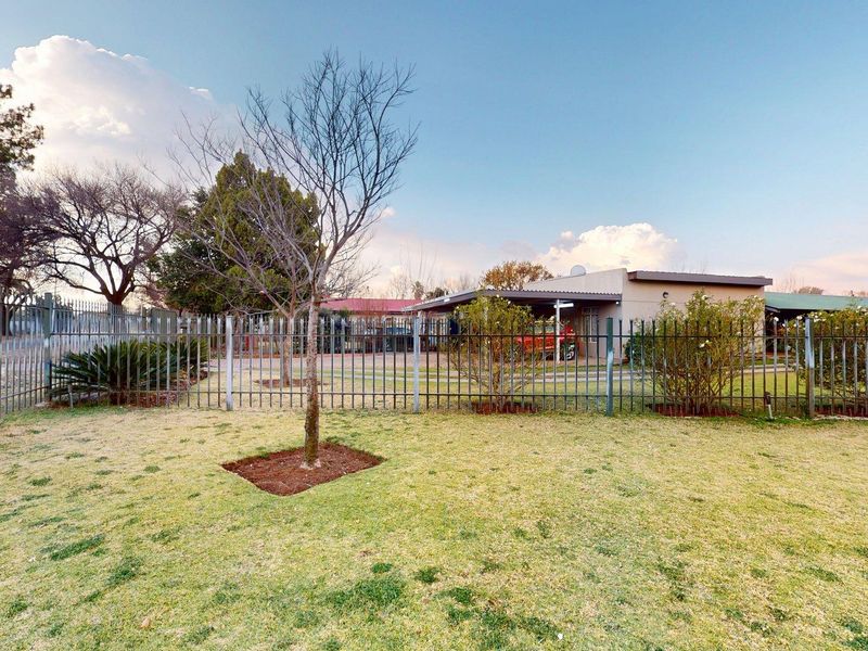 A spacious backyard featuring a well-maintained lawn, established trees, and secure metal perimeter fencing with a view of the covered patio area.