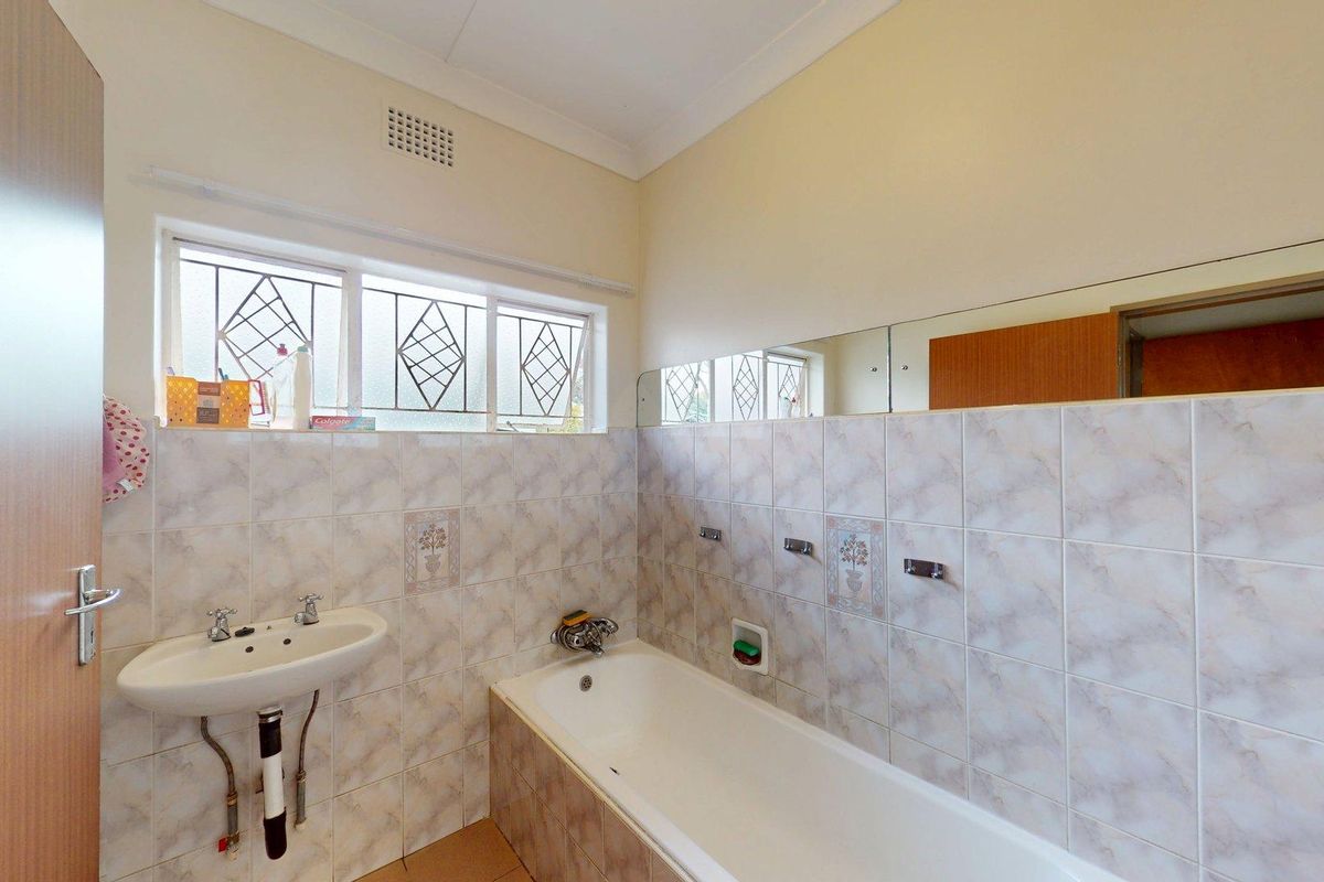 A functional bathroom featuring a built-in bathtub, wall-mounted basin, and tiled walls with a large vanity mirror and leaded glass window.