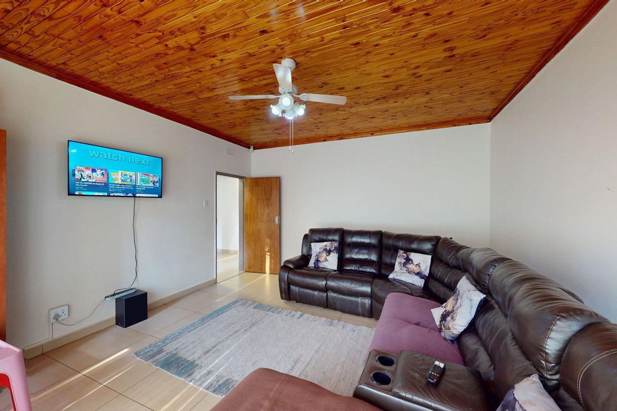 A living room featuring a distinctive timber tongue and groove ceiling, ceiling fan, and neutral tiled flooring.