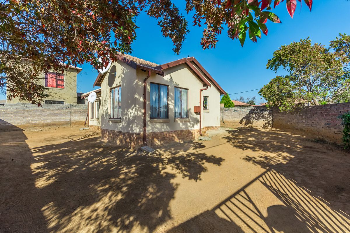 Rear view of the house featuring a tiled roof, stone cladding base, and a large, unlandscaped yard enclosed by a brick boundary wall.