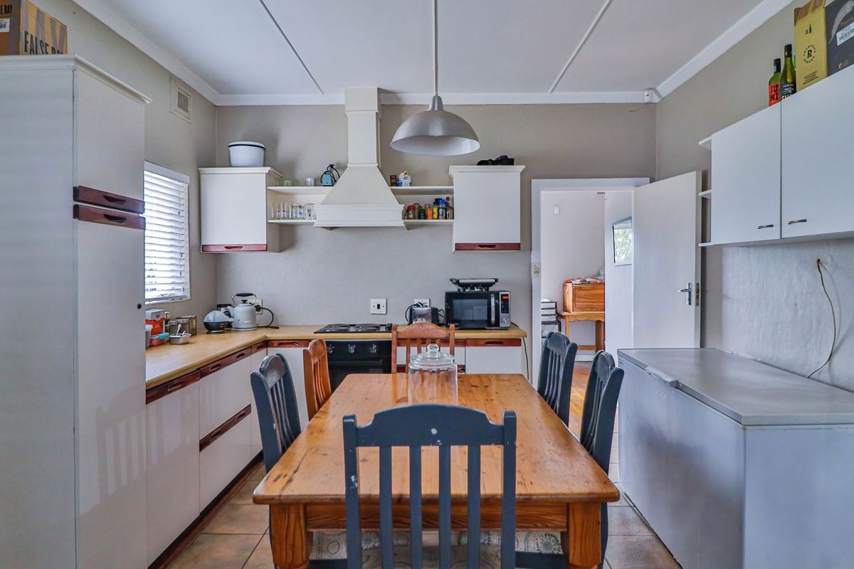 A functional kitchen featuring built-in cabinetry, a hob, an oven, and an extractor fan, with tiled flooring and a central dining area.