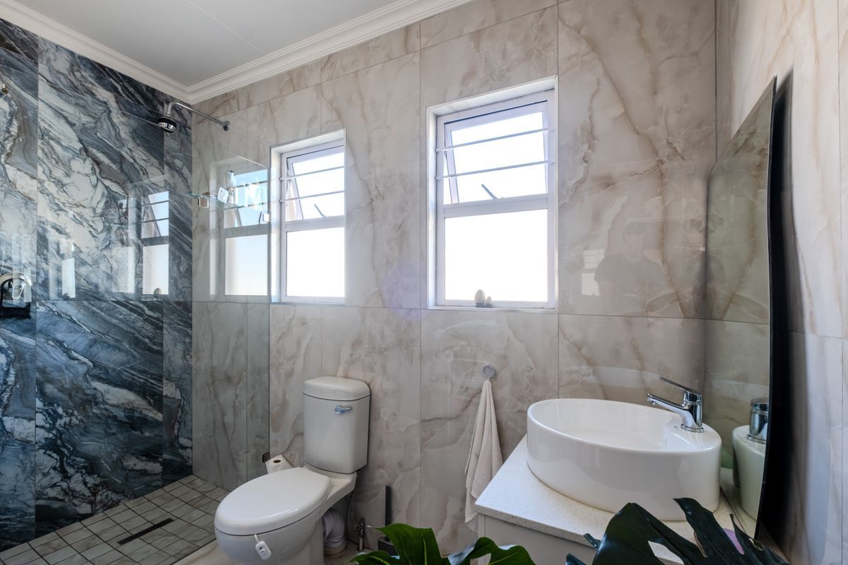 Modern bathroom featuring a walk-in shower with marble-effect tiling, a vessel sink on a stone vanity, and dual casement windows for natural light.
