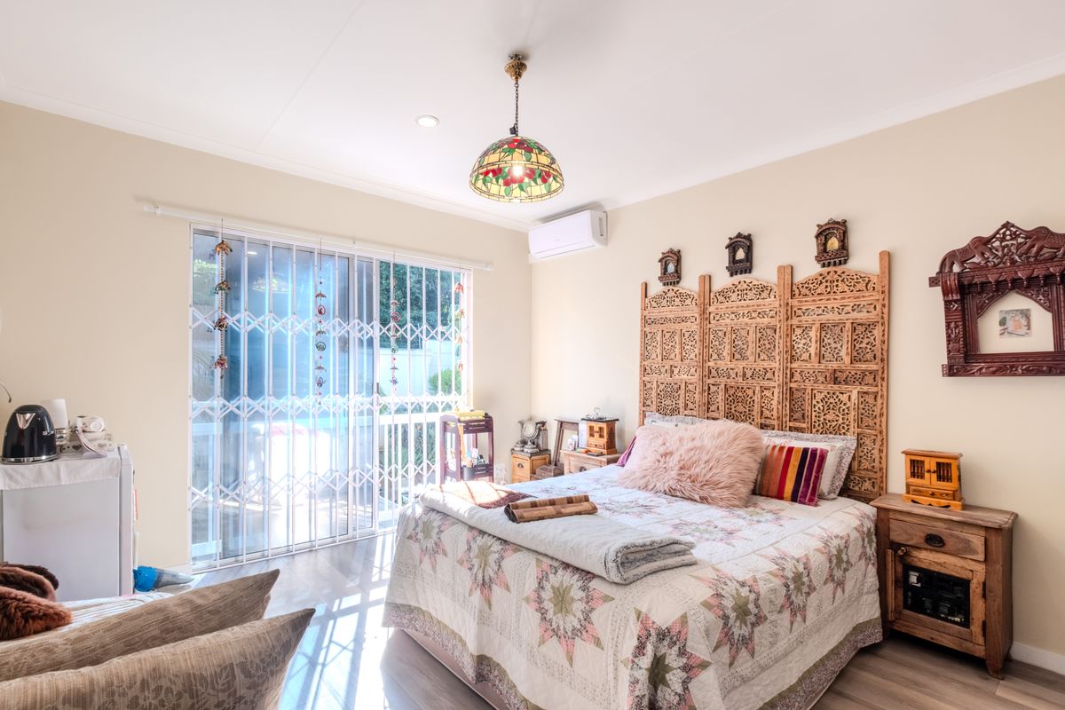 A well-maintained bedroom featuring laminate flooring, a split-system air conditioner, and a sliding glass door with a security gate leading to the exterior.