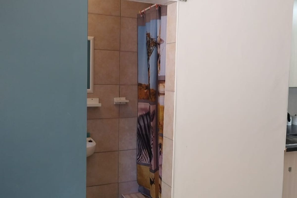 A compact bathroom featuring tiled walls and flooring, accessed via a modern sliding door, with a functional shower and basin area.