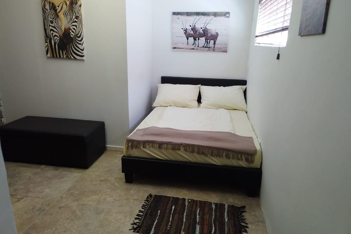 A compact bedroom featuring neutral tiled flooring and a window fitted with venetian blinds.