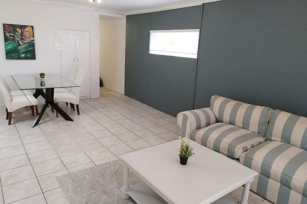 An open-plan living and dining area featuring neutral tiled flooring, a feature wall, and a built-in storage cupboard.