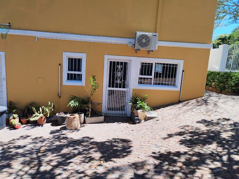 A paved rear courtyard area featuring a security gate, window security bars, and an external wall-mounted air conditioning unit.