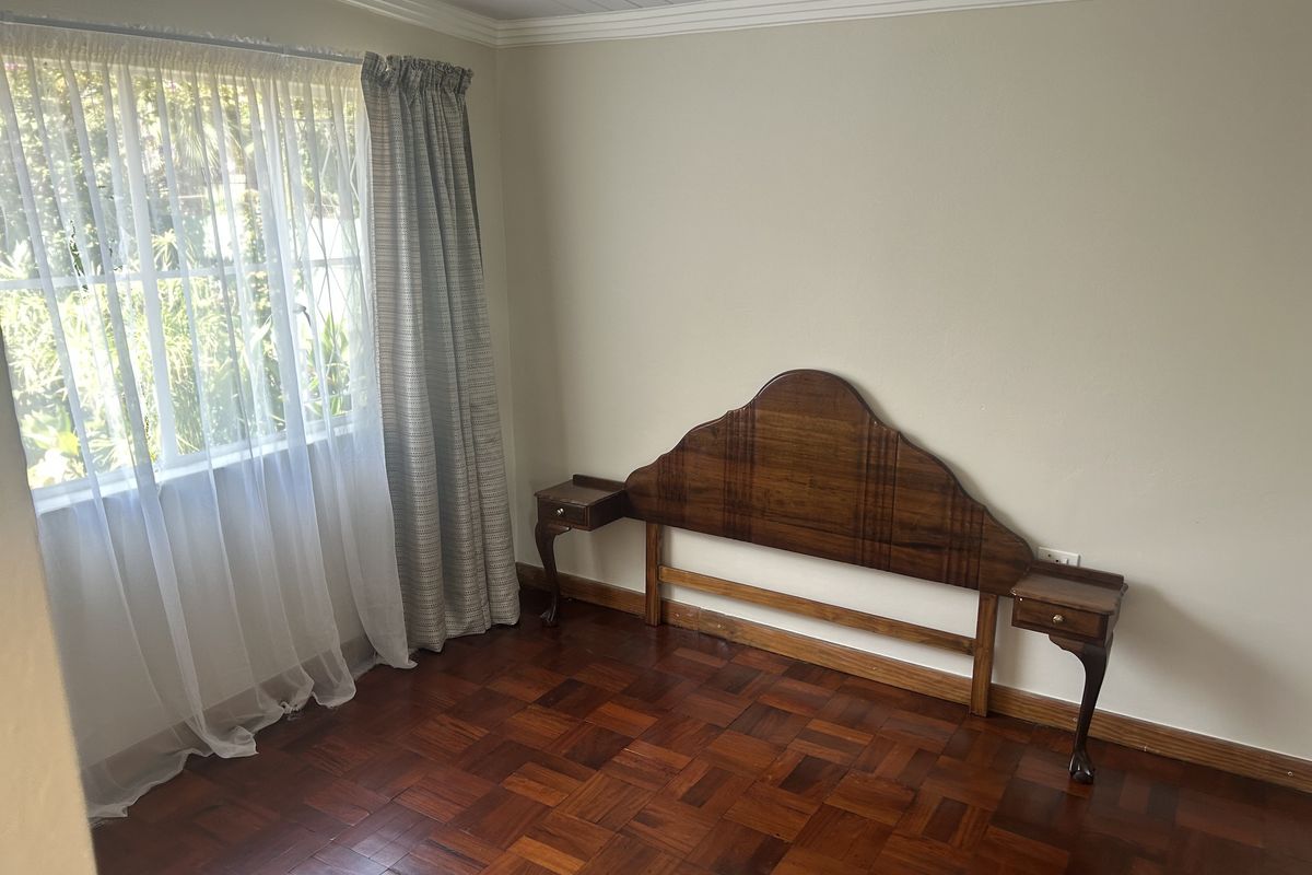 A bedroom featuring polished parquet flooring, neutral walls, and a built-in timber headboard with integrated side tables.