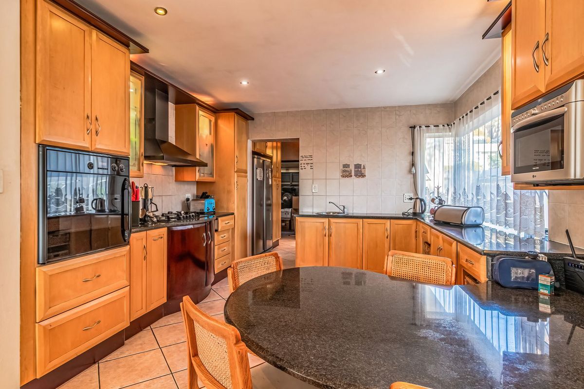 A spacious kitchen featuring warm-toned wooden cabinetry, granite countertops, built-in appliances, and a functional layout with an integrated dining area.