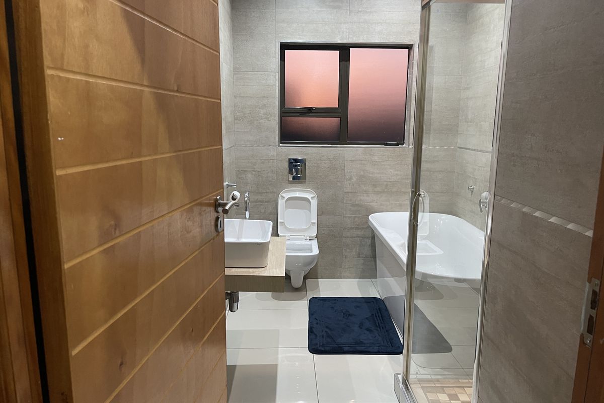 Modern bathroom featuring a wall-hung toilet, wall-mounted basin, freestanding bathtub, and a glass-enclosed shower with neutral floor-to-ceiling tiling.