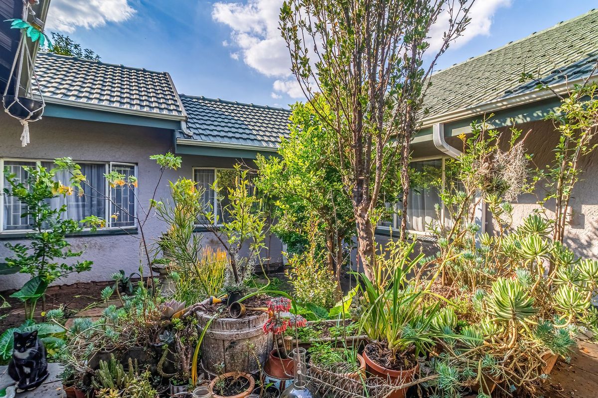 A view of the rear exterior of the house featuring a tiled roof, stucco walls, and security-fitted windows overlooking a landscaped garden area.
