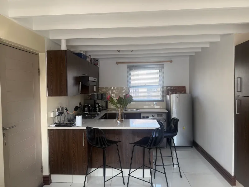 A functional kitchen featuring dark wood cabinetry, stone countertops, a breakfast bar, and exposed ceiling beams, finished with modern tiled flooring.