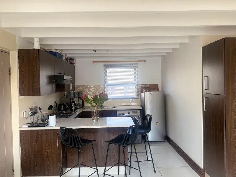 A functional kitchen featuring dark wood cabinetry, stone countertops, a breakfast bar, and exposed ceiling beams, providing a practical layout for daily use.