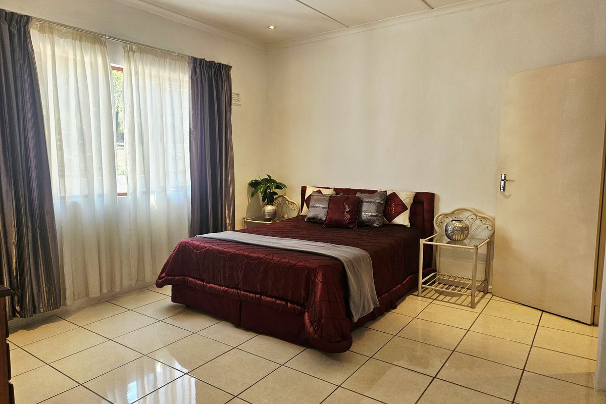 A spacious bedroom featuring neutral tiled flooring, recessed ceiling lighting, and large windows with installed curtain tracks.