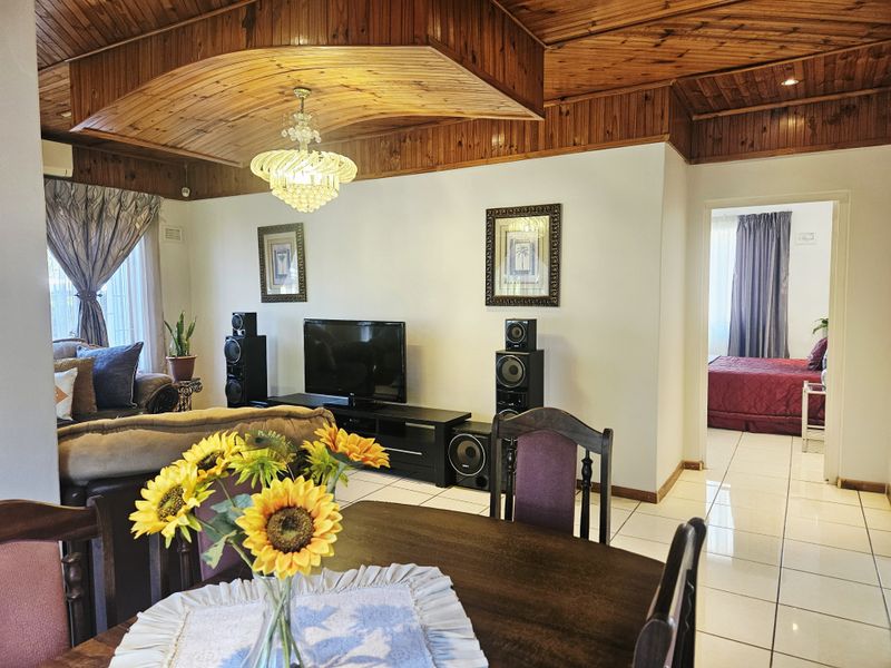 Open plan living and dining area featuring a distinctive vaulted timber ceiling, tiled flooring, and a central crystal chandelier.