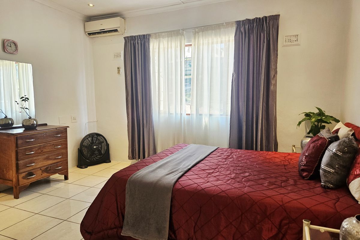 A well-maintained bedroom featuring tiled flooring, recessed downlighting, and a wall-mounted air conditioning unit.