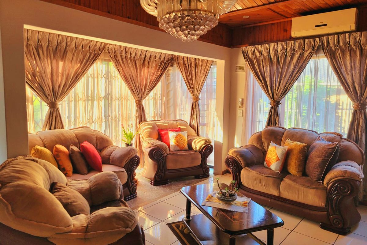 A cozy living room featuring a timber-paneled ceiling, crystal chandelier, split-system air conditioning, and large sliding glass doors that provide ample natural light.