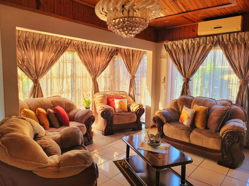 A cozy living room featuring a timber-paneled ceiling, crystal chandelier, split-system air conditioning, and large sliding glass doors that provide ample natural light.