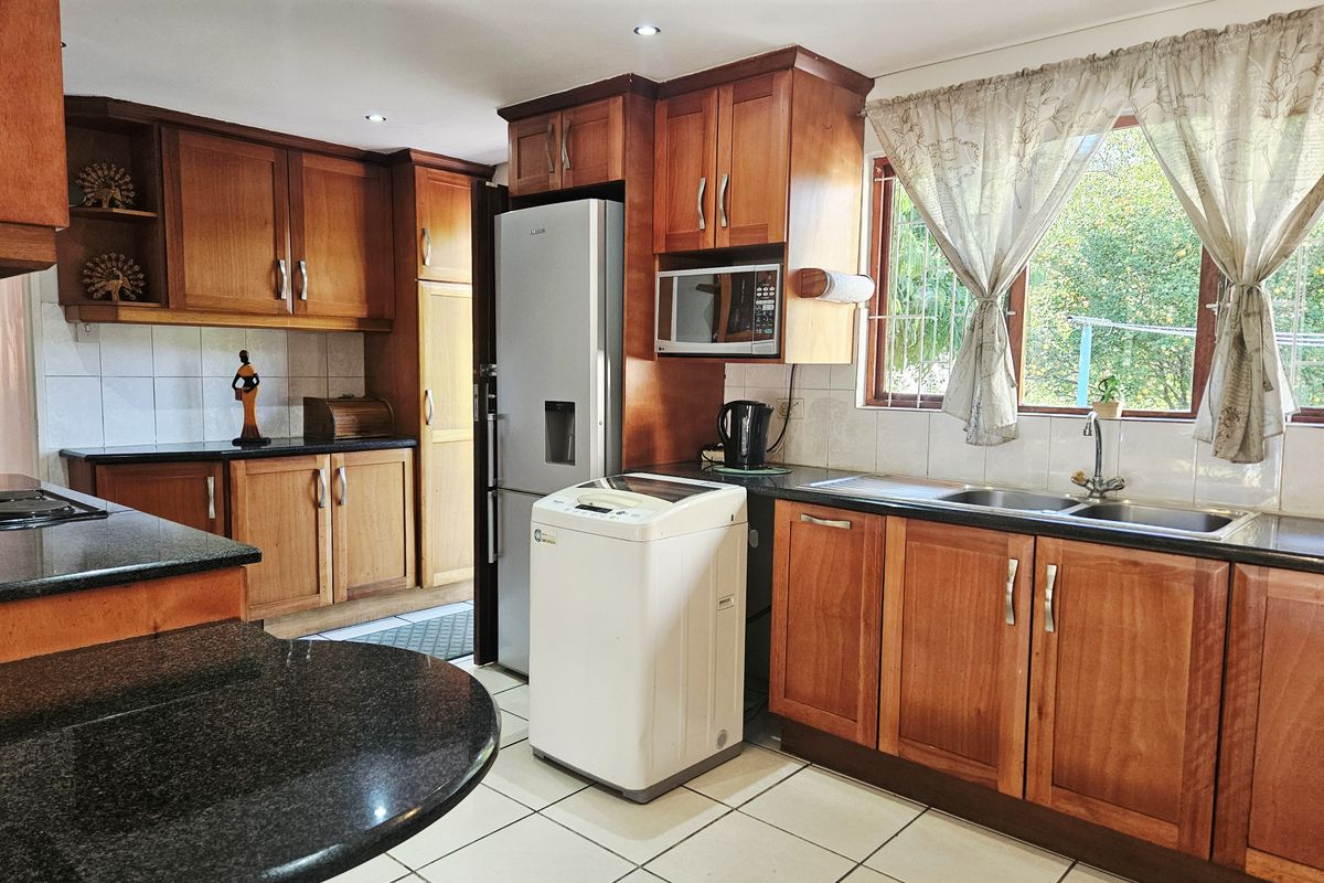 A functional kitchen featuring warm wooden cabinetry, granite countertops, a double basin sink, and tiled flooring with ample storage space.